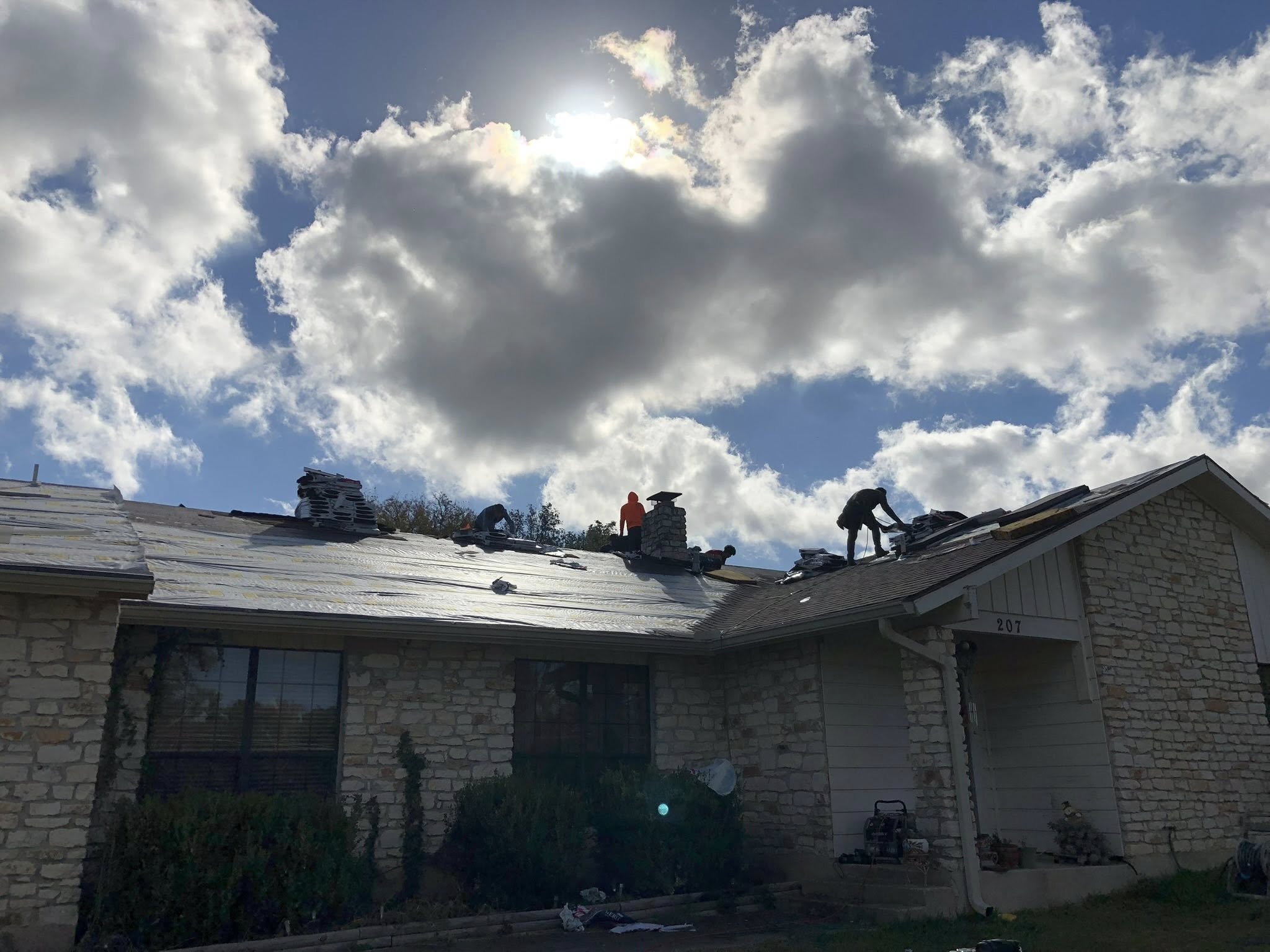 Roof replacement on a stone home with cloudy sky