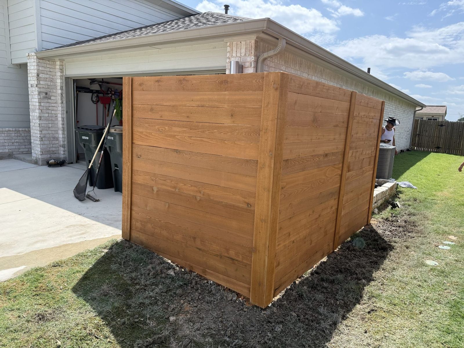 Horizontal cedar privacy screen built to hide trash bins and an AC unit beside a garage in Austin, TX