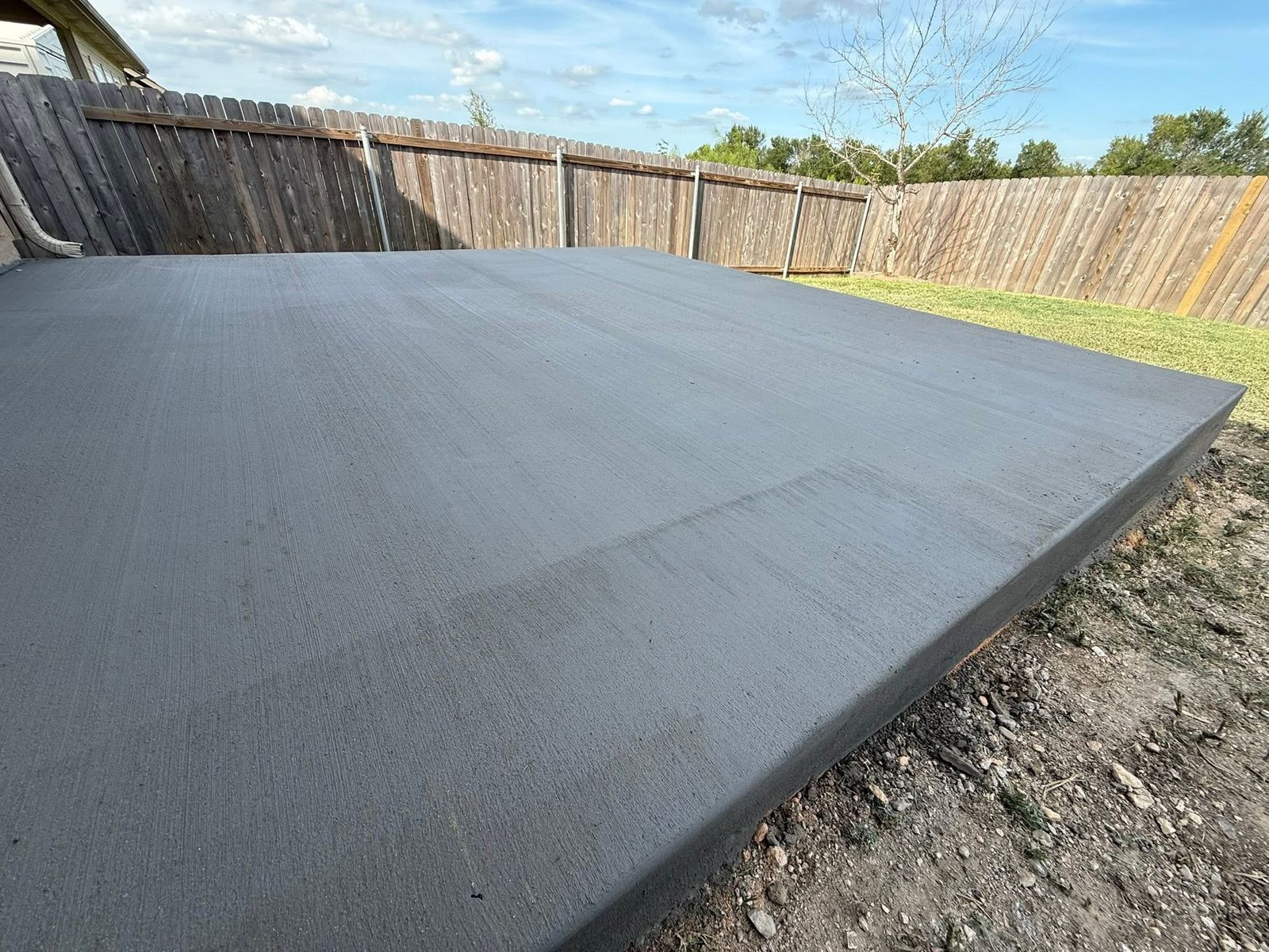 Finished broom-finish concrete patio slab in a fenced backyard in greater Austin, TX