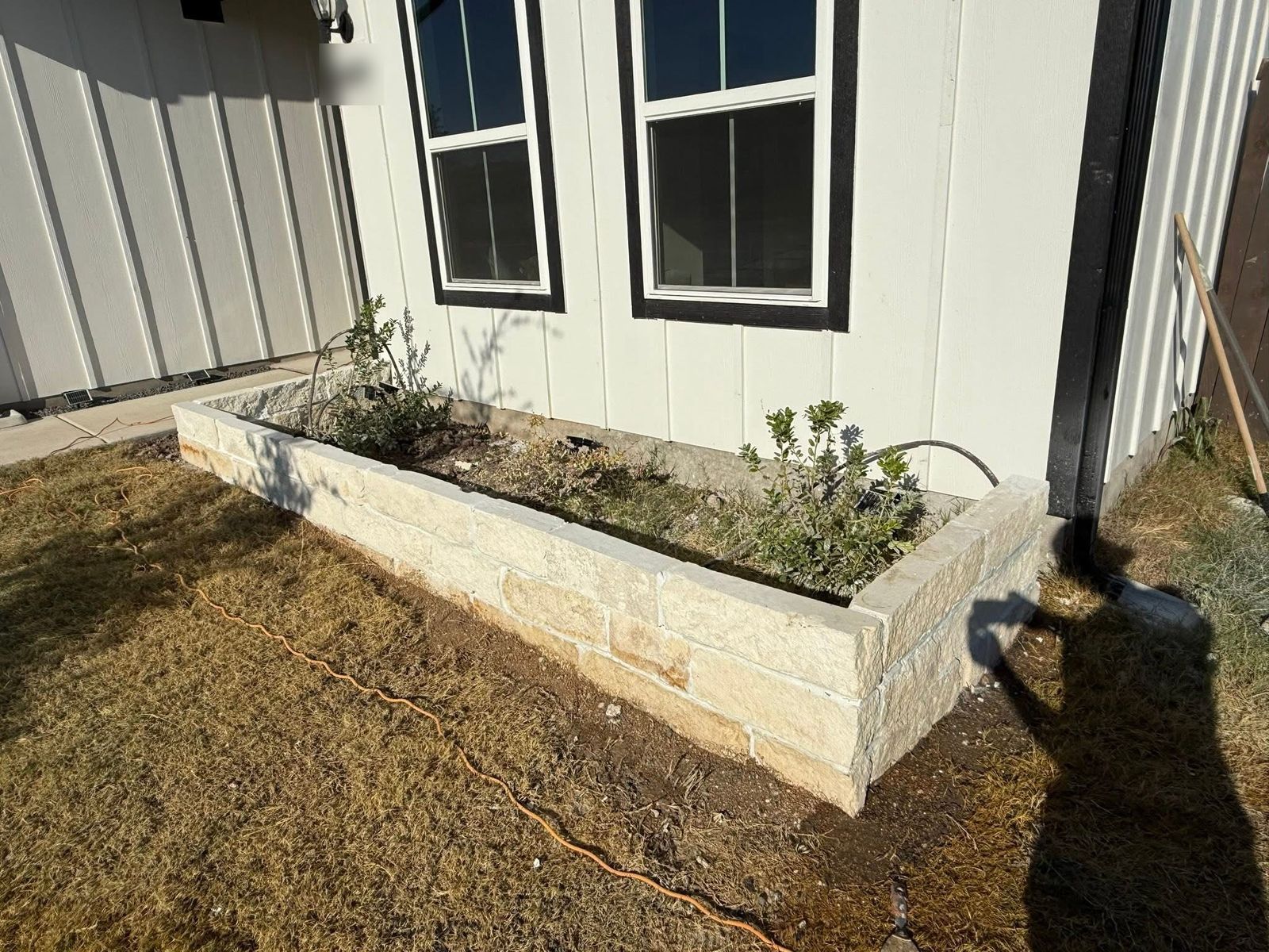 Cream limestone raised planter bed built along the front of a white board-and-batten home in Austin, TX