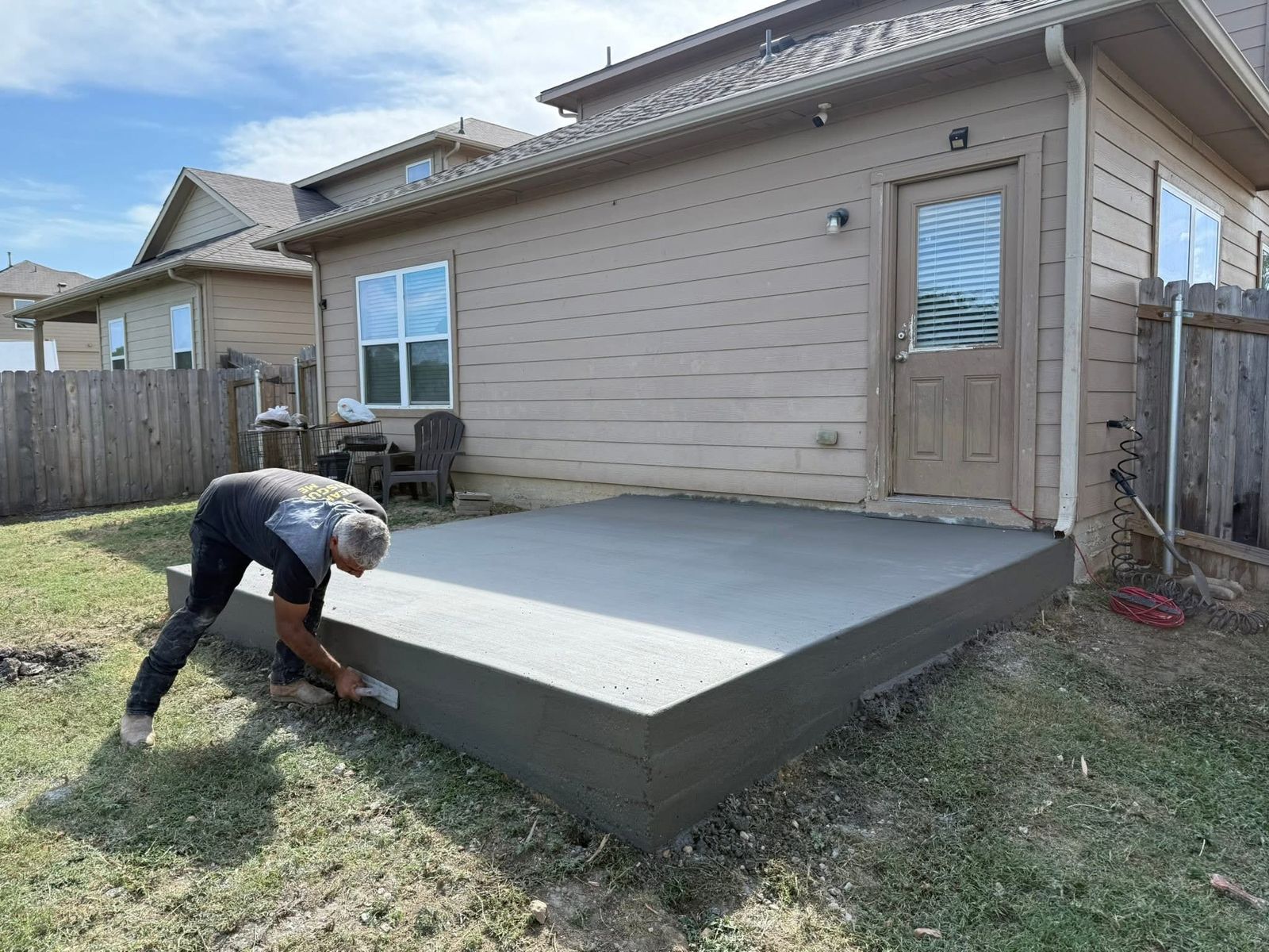 Concrete finisher edging a freshly poured raised concrete patio behind a home in greater Austin, TX