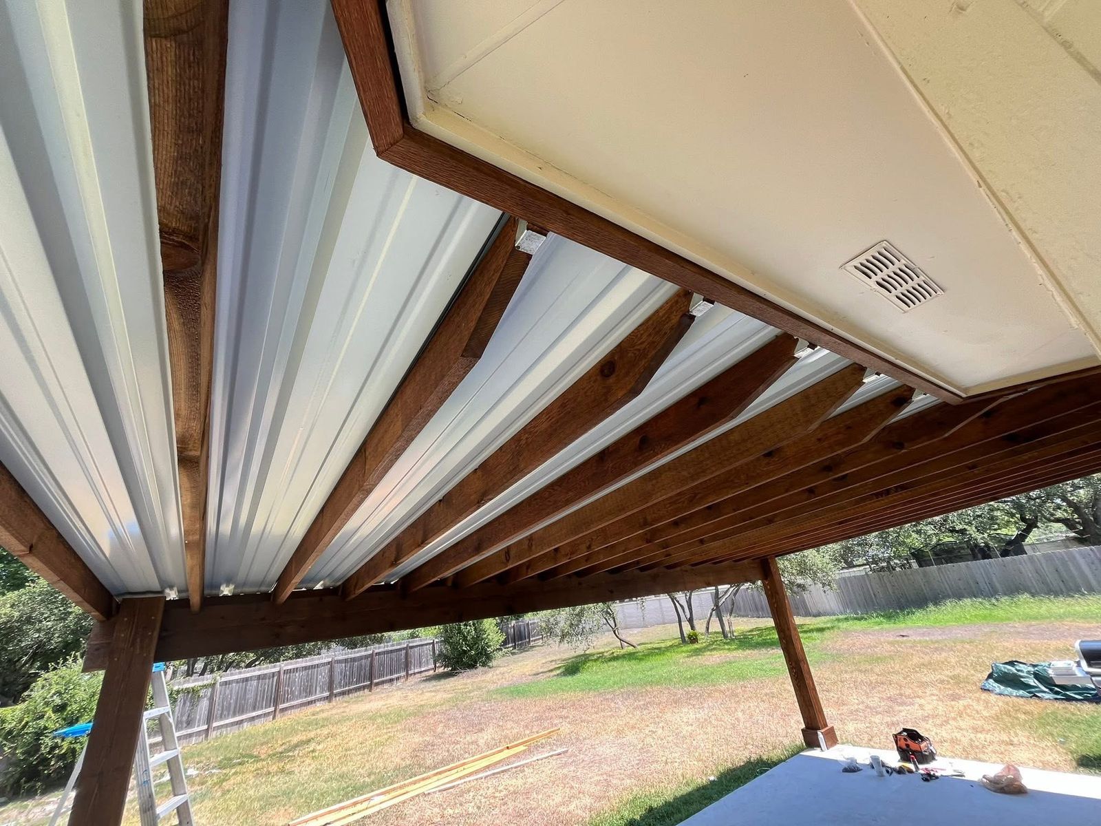 Underside of a stained cedar patio cover with a white metal roof tied into the house in Austin, TX