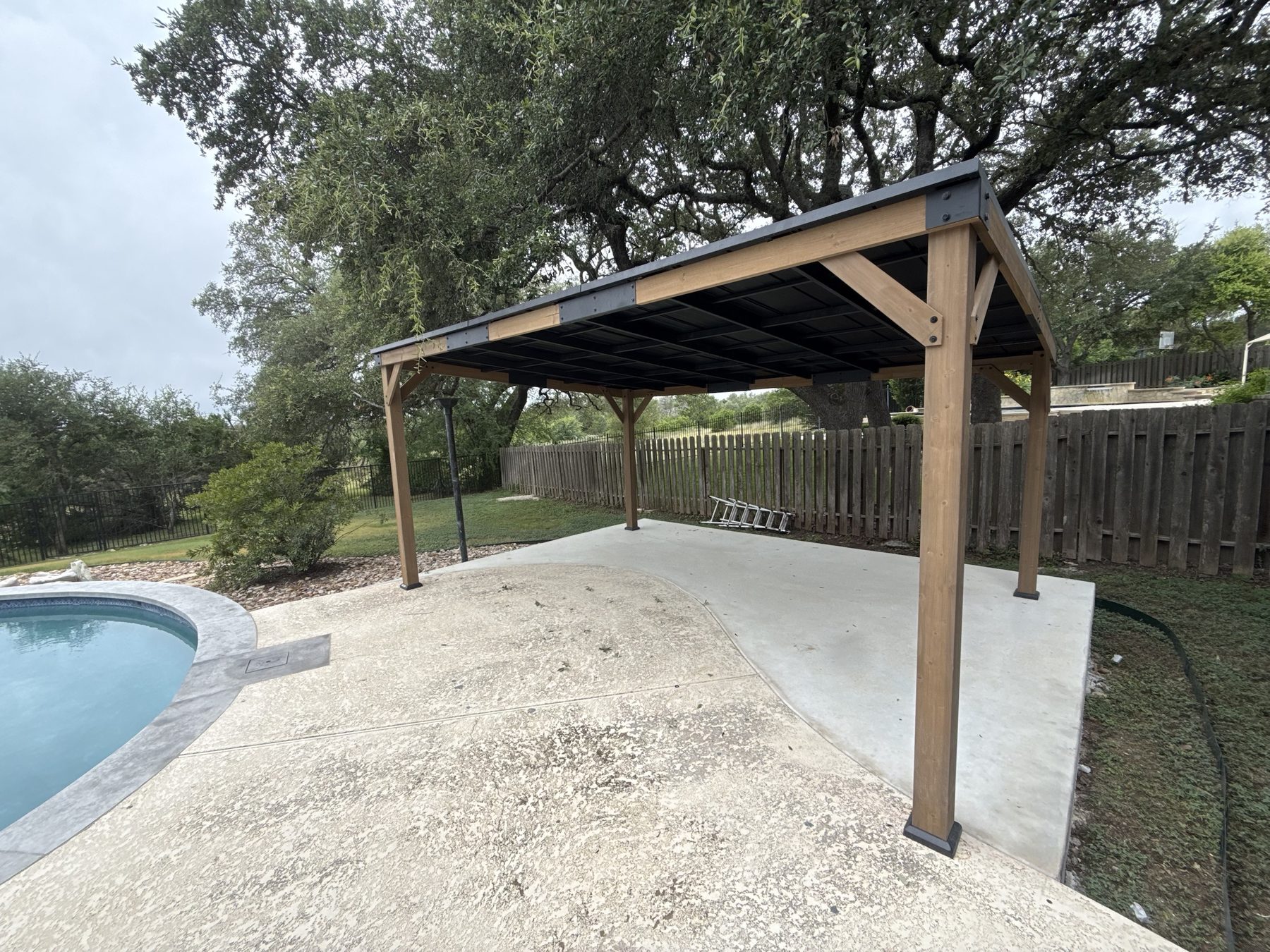 Cedar pavilion with a standing-seam metal roof beside a pool, built in the Austin area by JB Contracting ATX.