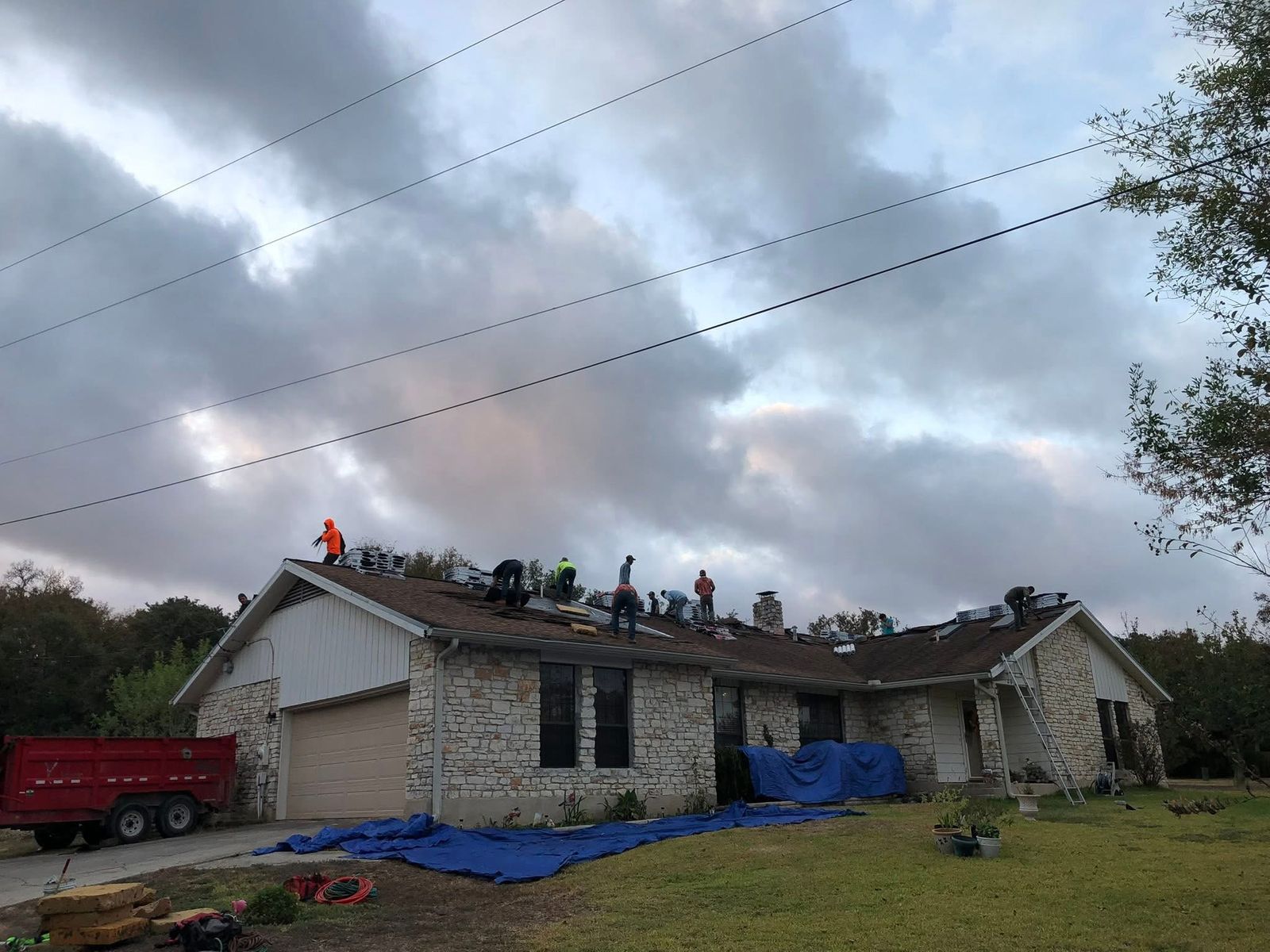Roofing crew tearing off and replacing the shingle roof on a stone ranch home near Austin, TX