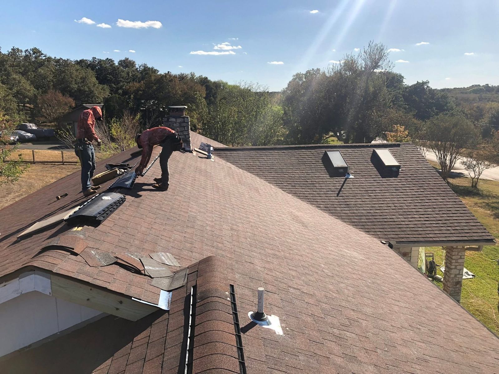 Roofers installing ridge vent on a new architectural shingle roof with skylights near Austin, TX