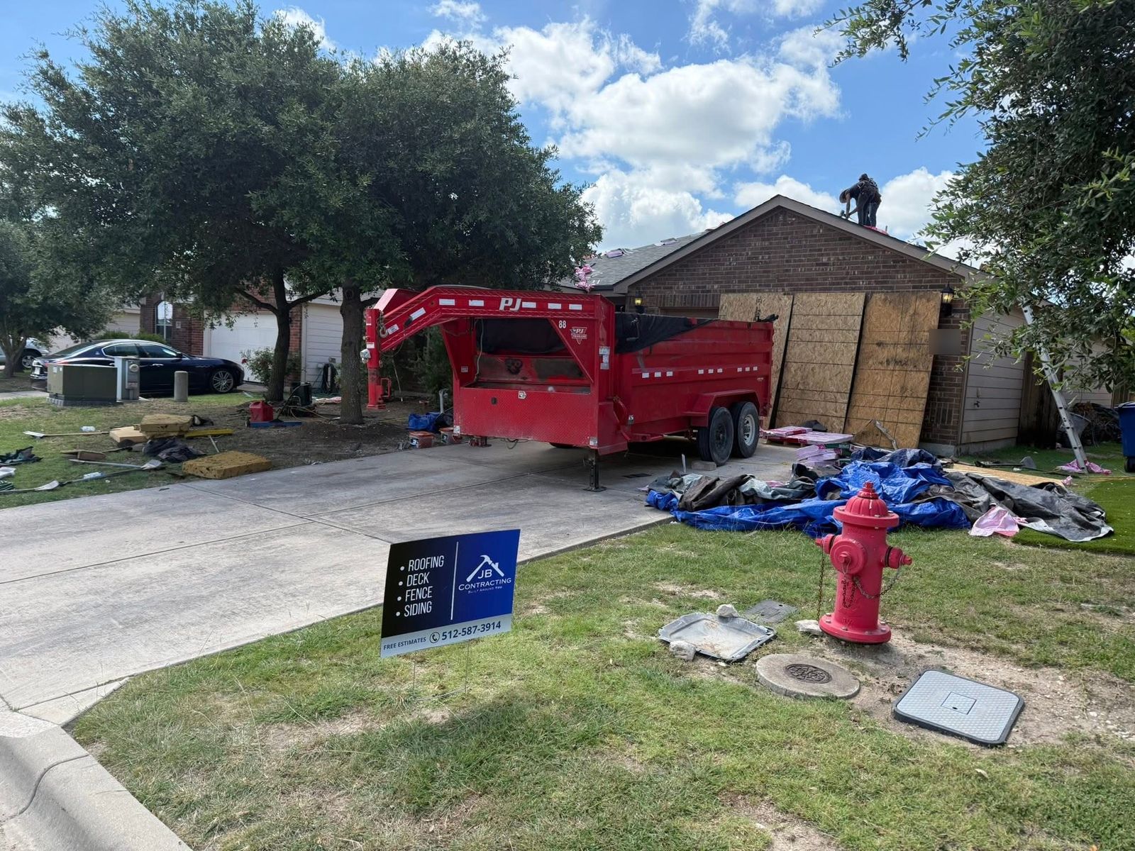 Roof replacement underway with a dump trailer in the driveway and a JB Contracting yard sign out front, Austin area